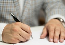 Zdjęcie dłoni trzymających długopis oraz podpisujących dokument