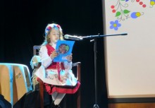 Dziewczynka w stroju kaszubskim siedzi przy mikrofonie i czyta