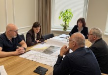 Pięć osób siedzi przy dużym, drewnianym stole na którym leżą rozłożone plany.