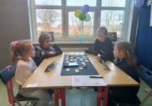 Czwórka dzieci przy stole grająca w Rummikub - powiększ