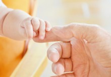 Dłoń niemowlęcia chwyta palec dłoni dorosłej osoby - powiększ