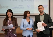 Dwie kobiety i mężczyzna. Po prawej stronie mężczyzna trzymający podpisany dokument. Po środku Burmistrz Gminy Żukowo, a po lewej kobieta, która patrzy w dół na dokumenty.  - powiększ