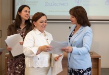 Trzy kobiety. Po prawej Burmistrz Gminy Żukowo przekazuje dokument kobiecie stojącej po środku.  - powiększ