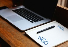 Laptop na biurku, koło niego notes i długopis na notesie. Na kartce napisane: NGO oraz logo Gminy Żukowo