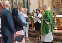 Uroczystość w kościele – grupa osób, w tym Burmistrz Mariola Zmudzińska, składa podziękowania kapłanowi ubranemu w zielony ornat. - powiększ