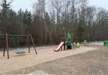 Zdjęcie przedstawia plac zabaw,  na którym widać huśtawkę Bocianie Gniazdo, konstrukcję zabawową ze zjeżdżalnią, huśtawkę ważkę.  - powiększ