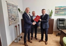 Trzy osoby, dwie z nich trzymają teczkę z umową - powiększ