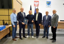 6 osób w sali obrad Rady Miejskiej w Żukowie. Burmistrz trzyma teczkę z umową.