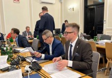 Na pierwszym planie dwóch mężczyzn przeglądających papiery. W tle widać innych uczestników spotkania.  - powiększ