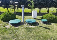 Przydomowa oczyszczalnia ścieków – trzy komory z zielonymi włazami, odpowietrznik i skrzynka sterująca, wkomponowane w ogród. - powiększ