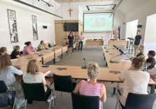 Szkolenie lub spotkanie w sali konferencyjnej z prezentacją multimedialną i uczestnikami siedzącymi przy stołach. - powiększ