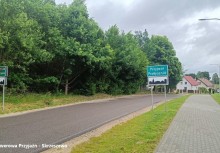 Na zdjęciu ulica, nowopowstała ścieżka rowerowa, po lewej stronie zdjęcia widoczne drzewa i w oddali zabudowania mieszkalne.  - powiększ