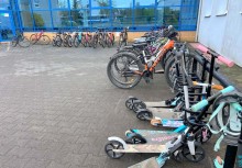 Hulajnogi i rowery zaparkowane przed budynkiem szkoły. - powiększ