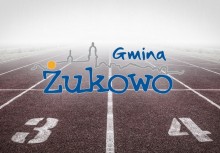 Na pierwszym planie logo Gminy Żukowo. W tle bieżnia lekkoatletyczna