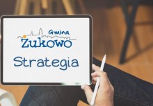 Osoba trzymająca tablet, a na nim logo Gminy Żukowo i napis Strategia - powiększ