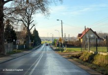 Na zdjęciu ulica, dwa samochody jadące w przeciwnych kierunkach, po prawej zabudowania mieszkalne.   - powiększ