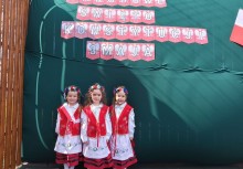 Trzy dziewczynki z przedszkola w Miszewie ubrane w kaszubskie stroje ludowe pozują na tle dekoracji z napisem „Narodowe Święto Konstytucji 3 Maja” – uroczysty występ z okazji święta państwowego. - powiększ