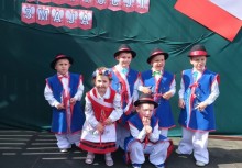Grupa dzieci z przedszkola w Miszewie w kaszubskich strojach ludowych pozuje na tle dekoracji z okazji Święta Konstytucji 3 Maja – chłopcy w niebieskich kamizelkach i kapeluszach, dziewczynka w czerwonym gorsecie. - powiększ