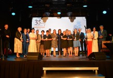 Grupowe zdjęcie nagrodzonych uczestników gali z okazji 35-lecia samorządu – elegancko ubrani, stoją na scenie na tle prezentacji jubileuszowej. - powiększ