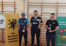 Trzech mężczyzn z pucharami, stojących na tle banerów Urzędu Marszałkowskiego i Pomorskiego Zrzeszenia LZS – uroczystość sportowa.








 - powiększ