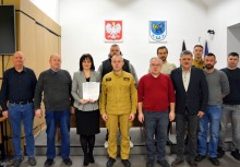 Grupowe zdjęcie z Burmistrz Mariolą Zmudzińską i przedstawicielami służb oraz mieszkańcami – wręczenie podziękowań w sali Urzędu Gminy w Żukowie, w tle godło Polski i herb gminy. - powiększ
