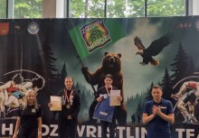 Dwóch młodych medalistów na podium z dyplomami, na tle grafiki z niedźwiedziem i orłem – uroczystość zakończenia zawodów zapaśniczych. - powiększ