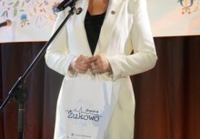 Kobieta w białej marynarce przemawia przy mikrofonie, trzymając torbę z logo Gminy Żukowo. W tle widoczny kolorowy baner z motywami kaszubskimi.









 - powiększ