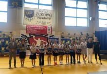 Uroczyste wręczenie nagród – grupa uczennic w strojach sportowych i nauczycieli pozuje z dyplomami i pucharami. W tle baner „Gmina Żukowo” i napis „Gminny Konkurs Wiedzy o Młodzieży i Środowisku”. - powiększ