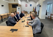 Grupa osób siedzi przy stole na Sali Rady Miejskiej. W tle widać baner Gminy Żukowo, godło Polski oraz herb Gminy Żukowo.