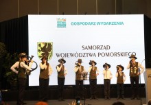 Grupa dzieci gra na instrumentach. W tle widać duży baner z napisem 'GOSPODARZ WYDARZENIA - SAMORZĄD WOJEWÓDZTWA POMORSKIEGO'.  - powiększ