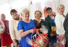 Na zdjęciu sześć kobiet. Na pierwszym planie kobieta w niebieskiej sukni trzyma kosz prezentowy - powiększ