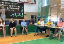 jury konkursu za stołem - 3 panie,  dzieci odpowiadające na pytania, sala gimnastyczna, konkurs kaszubski wiec 2021 - powiększ