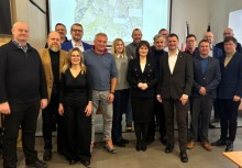 Grupa siedemnastu osób. Za nimi wyświetlona mapa  - powiększ