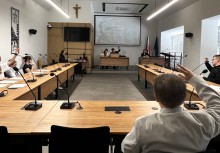 Uczestnicy Sesji podnoszą rękę w górę w trakcie głosowania. W tle widać rzutnik z napisem 'OTWARCIE IV SESJI VI KADENCJI MŁODZIEŻOWEJ RADY GMINY W ŻUKOWIE'.  - powiększ