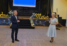 Kobieta i mężczyzna stoją przed sceną. Kobieta przemawia do mikrofonu.  - powiększ