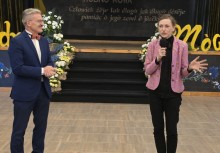 Kobieta i mężczyzna stoją przed sceną. Kobieta przemawia do mikrofonu.  - powiększ