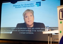 Kadr z nagrania wyświetlonego na rzutniku, na którym widać prelegentkę oraz logo Alliance for Scientific Autism Intervention.  - powiększ