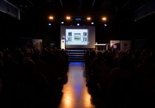 Widok na sale pełną widzów. Na scenie przy mównicy stoi prelegentka, a w tle widać prezentację wyświetloną na rzutniku.  - powiększ